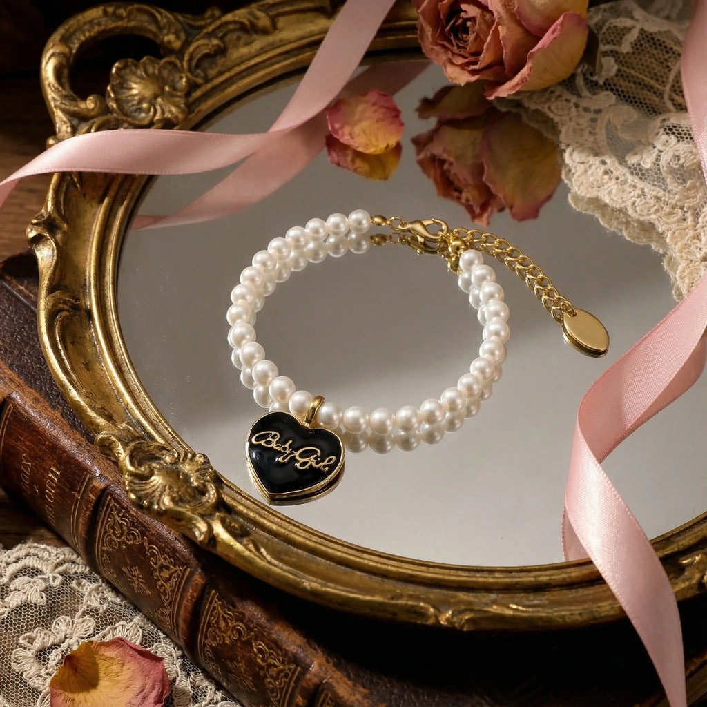Classic single strand pearl bracelet featuring a black enamel heart charm with gold Babygirl script by Selviora