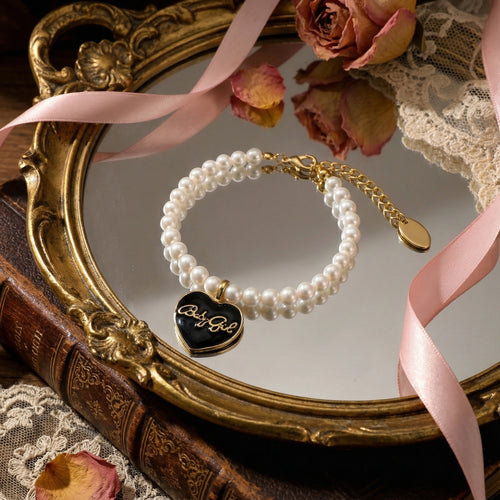 Classic single strand pearl bracelet featuring a black enamel heart charm with gold Babygirl script by Selviora
